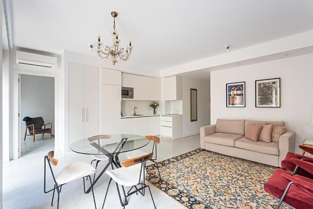 A modern living room with a glass dining table, a sofa, and a patterned rug.