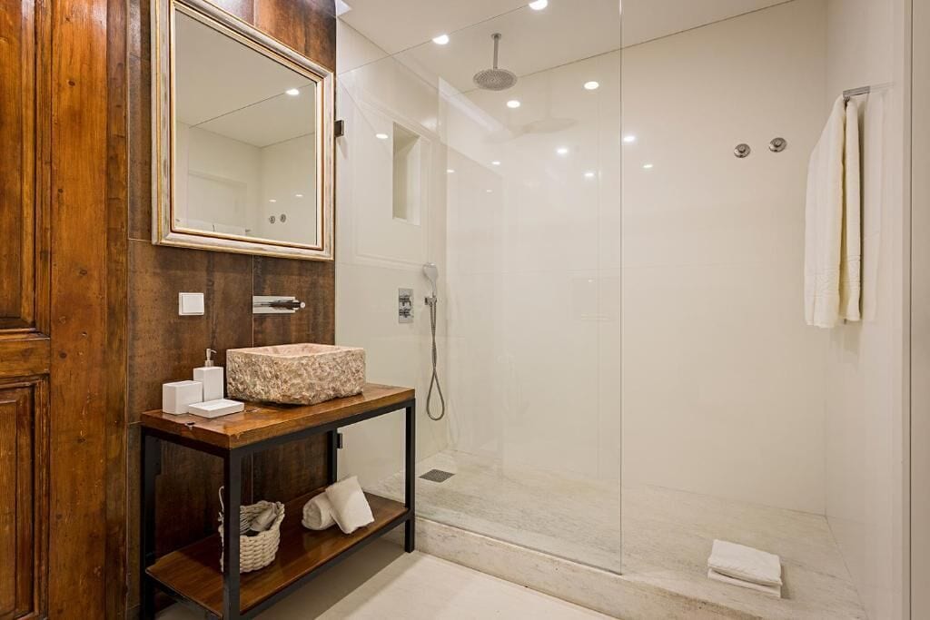 A bathroom with a wooden vanity, a large mirror, a shower with a glass door, and a white towel hanging on the wall.
