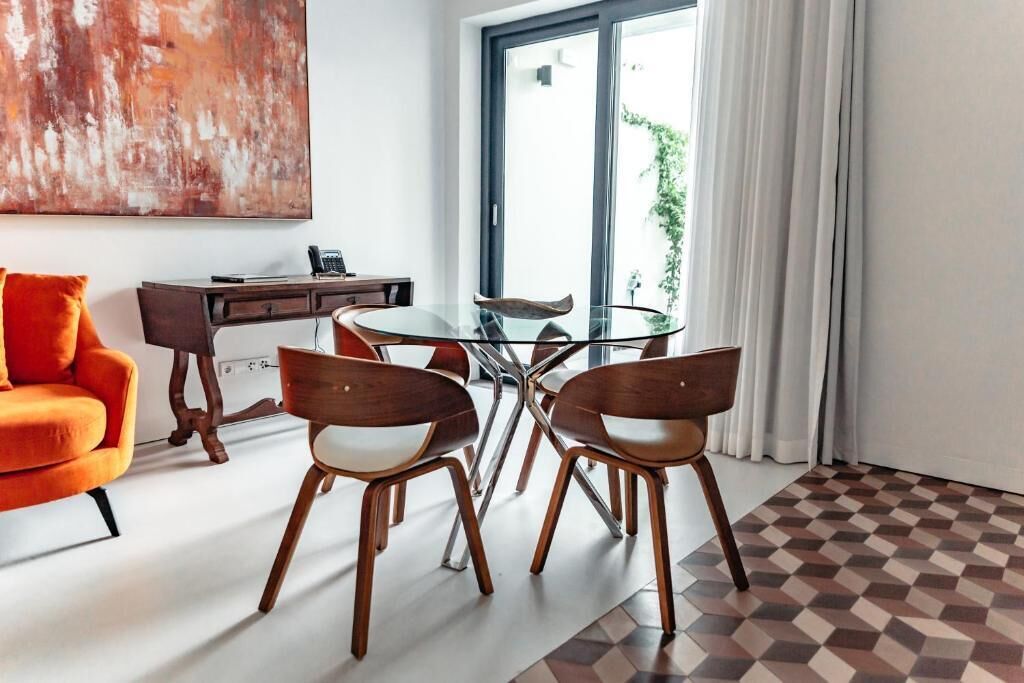 A modern living room with a glass table, wooden chairs, a sofa, and a desk with a telephone.