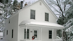 Ein weißes, zweistöckiges Haus mit Veranda, Nummer 10, umgeben von schneebedeckten Bäumen.
