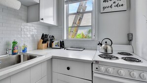 Una cocina con armarios blancos, un lavamanos de acero inoxidable, una estufa y una ventana con vistas al verdor exterior.