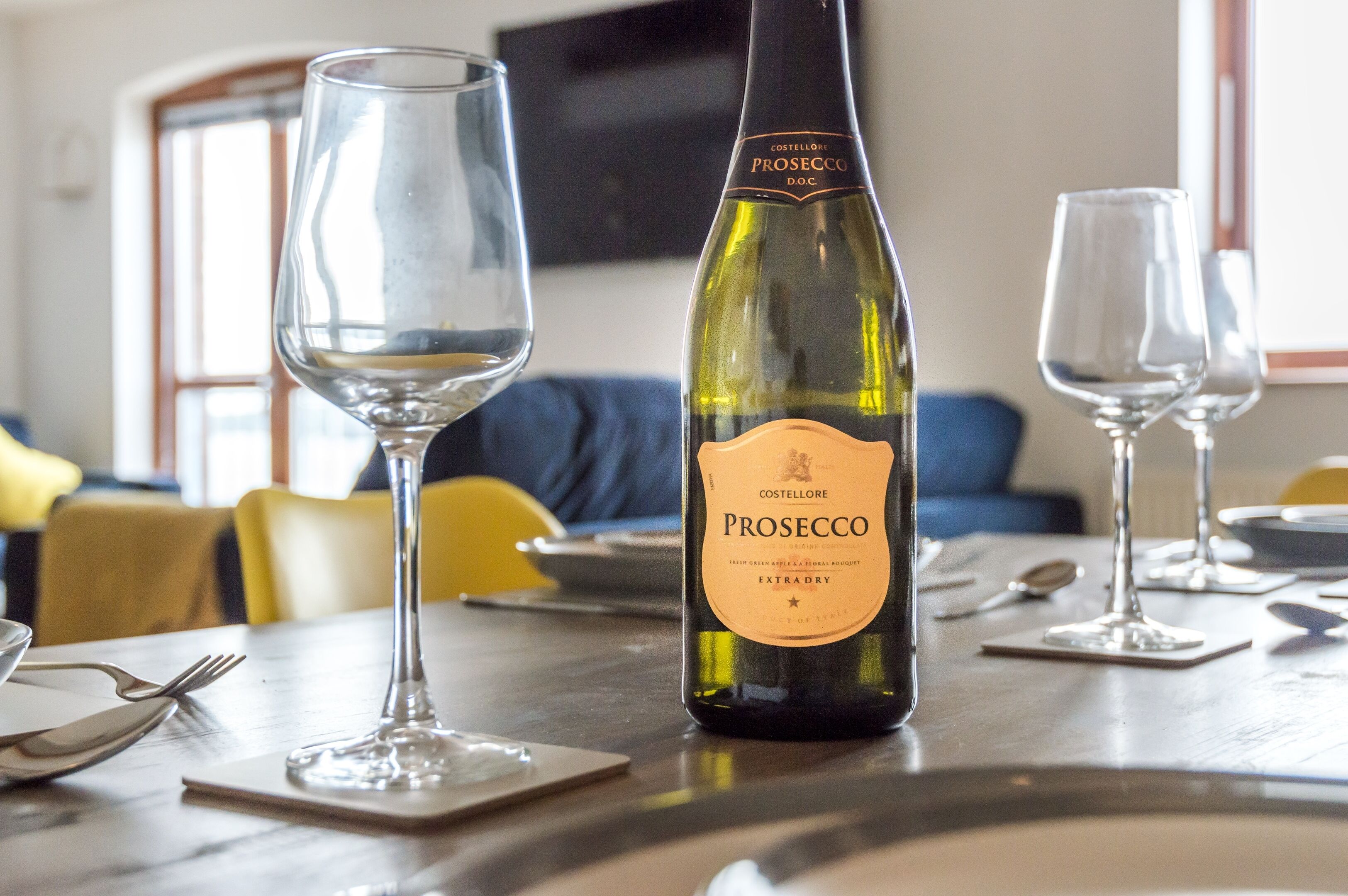 A bottle of Prosecco DOC wine on a table with two empty wine glasses.
