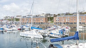 A marina with multiple boats docked, surrounded by buildings with brick facades and large windows.