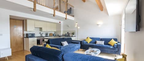 Una sala de estar moderna con sofás azules, una cocina al fondo y una escalera de madera.