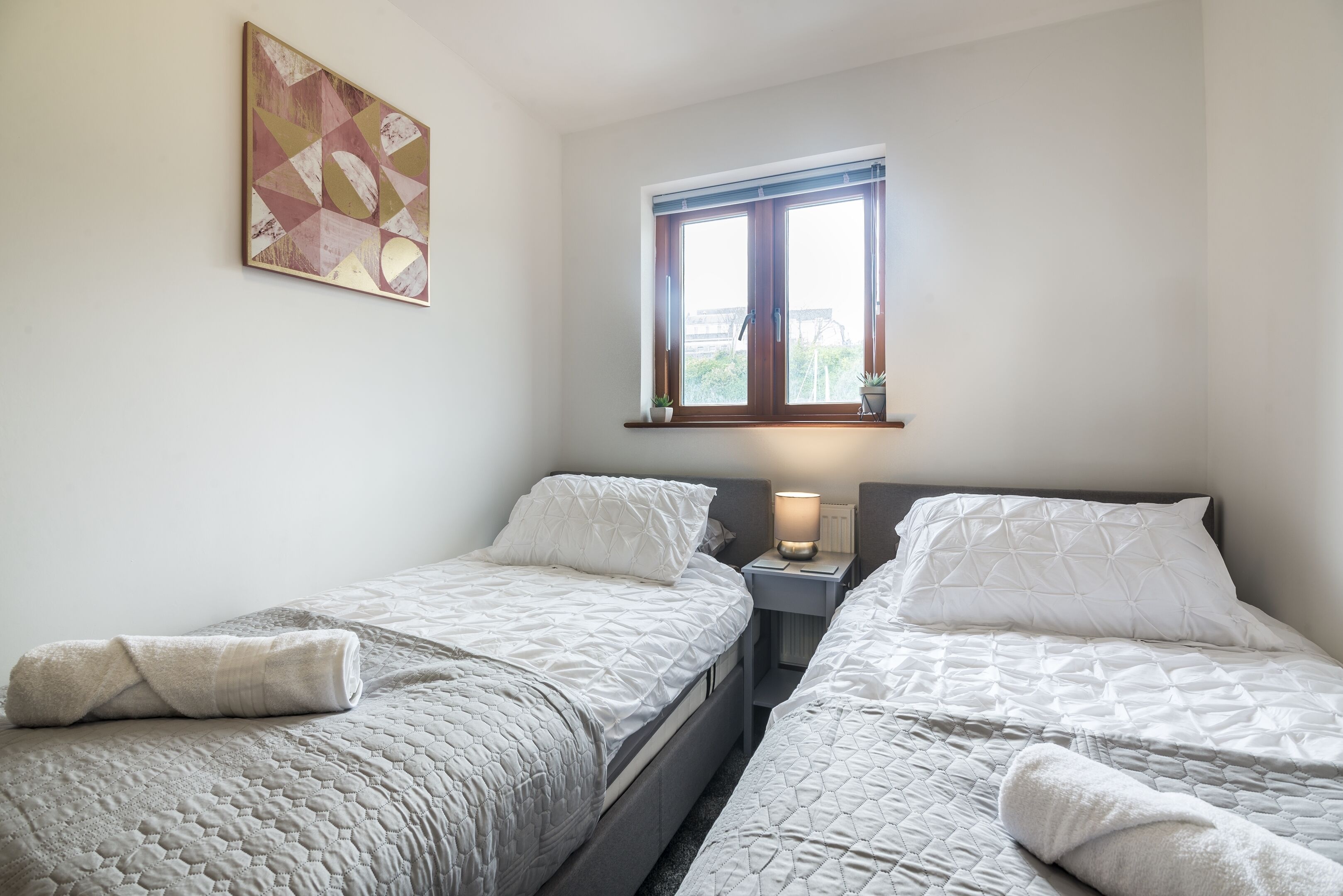 A bedroom with two beds, a window, and a painting on the wall.
