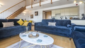 A spacious living area with two dark blue sofas, a marble coffee table, and a wooden staircase.