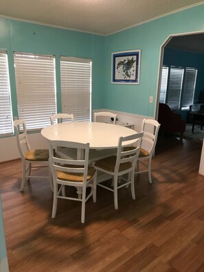 A dining area with a round table and six chairs, light blue walls, and wooden flooring.