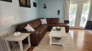 Una sala de estar con un sofá seccional de cuero marrón, una mesita de centro blanca y una pequeña mesa auxiliar de madera.
