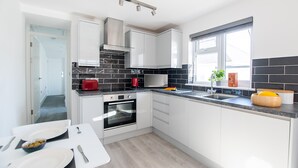 A modern kitchen with white cabinets, a black tiled backsplash, a red kettle, and a window with a view.