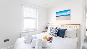 A neatly made bed with white linens, a tray with croissants and fruit, and a beach scene painting on the wall.