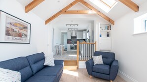 A modern living room with two sofas, a wooden staircase, and a kitchen in the background.