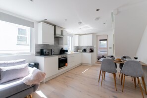 Una cocina moderna con armarios blancos, horno empotrado y comedor con mesa y sillas.