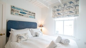 A neatly made bed with white linens and rolled towels, a blue headboard, and a wall with nautical-themed artwork. - Stone’s Throw, Central St Ives – Sleeps 7 – Dog Friendly (St Ives)