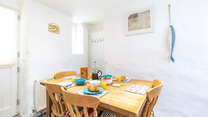 A dining area with a wooden table, chairs, and breakfast items including croissants, orange juice, and a coffee pot. - Stone’s Throw, Central St Ives – Sleeps 7 – Dog Friendly (St Ives)
