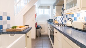 A modern kitchen with a blue and white checkered backsplash, stainless steel appliances, and a wooden cutting board with vegetables. - Stone’s Throw, Central St Ives – Sleeps 7 – Dog Friendly (St Ives)