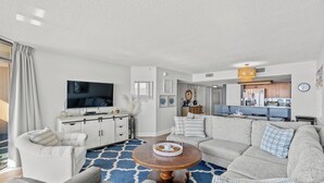 A modern living room with a large flat-screen TV, a round coffee table, and a sofa set. - Verandas 301 - Ocean Front - Luxury 4 Bed/3 Bath Condo (North Myrtle Beach)