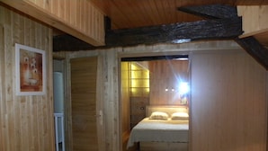 Un dormitori amb sostre de fusta, un llit amb roba de llit blanca i una porta que condueix a una altra habitació.