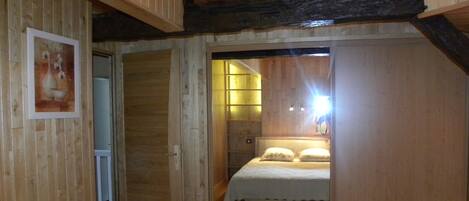 A bedroom with a wooden ceiling, a bed with white bedding, and a door leading to another room.