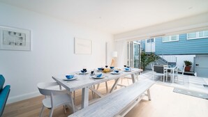 A modern dining area with a white table set for four, a bench, and a view of the backyard.