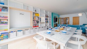 A modern living room with a dining area, white furniture, and a bookshelf filled with books and storage bins.