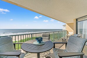 Ein Balkon mit Tisch, Stühlen und einem dekorativen Gegenstand. Blick auf Strand und Meer.