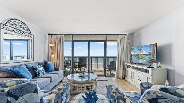 A living room with a sofa, chairs, a coffee table, a TV, and a balcony with a view.