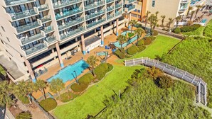 An aerial view of a hotel with multiple balconies, a swimming pool, and landscaped areas.