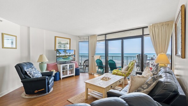 Una sala de estar con sofá, sillón, mesa de centro y vista al mar a través de amplias ventanas.