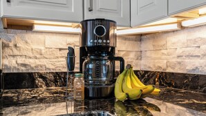 Una cocina con una cafetera, un tarro de canela y un racimo de plátanos sobre la encimera.