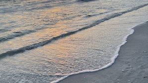 Ein Strand mit sanft anschwellenden Wellen und einem Sonnenuntergang im Hintergrund.