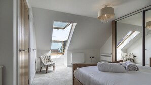 Ein Schlafzimmer mit einem großen Bett, einem Sessel, einem Spiegel und Dachfenstern.