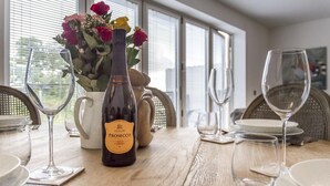 Ein Esstisch mit einer Prosecco-Flasche, einem Blumenstrauß und leeren Weingenüssen.