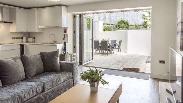 Ein modernes Wohnzimmer mit Sofa, Couchtisch, Essbereich mit Stühlen und Küchenzeile.