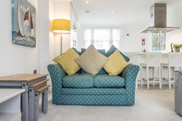 Sala de estar com um sofá azul-turquesa estampado com bolinhas, uma mesinha de madeira e um abajur.