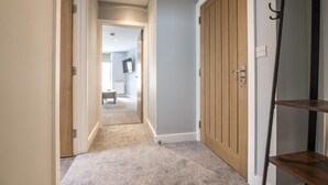 A hallway with a carpeted floor, wooden doors, and a shelf unit. - Tipyn O Haul - 1 Bedroom Apartment - Tenby (Tenby)