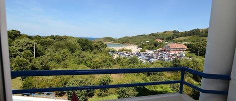 A balcony with a view of a beach, parking lot, and surrounding greenery.