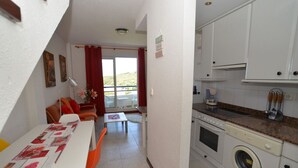 Une cuisine compacte équipée d’un lave-linge, un coin repas avec une table et des chaises, et une vue sur un balcon extérieur, accessible par une porte vitrée.