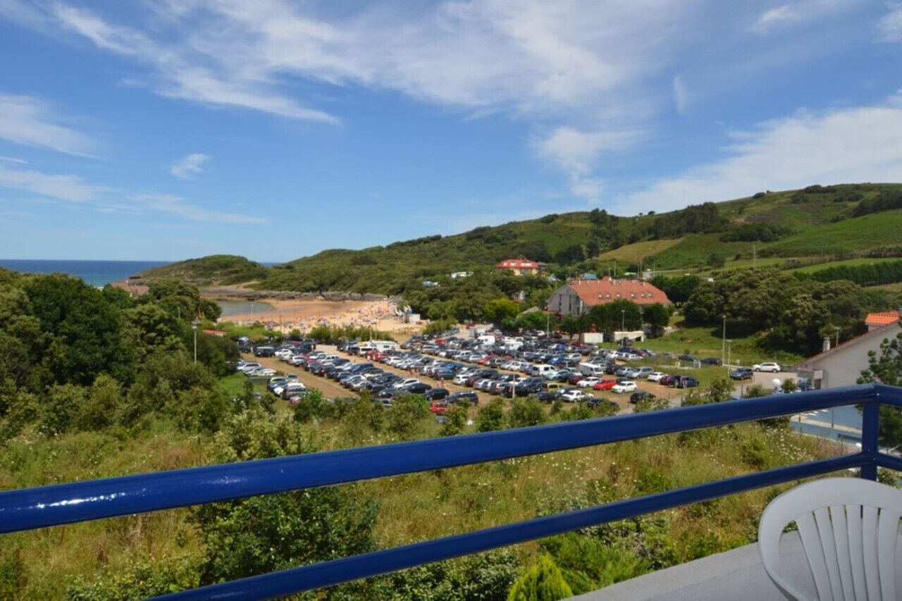 A view from a balcony overlooking a parking lot and a beach, with a red-roofed building in the background.