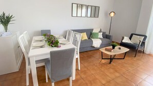 Ein Wohnzimmer mit Esstisch für zwei Personen, einem grauen Sofa, einem Couchtisch und einer Stehlampe.