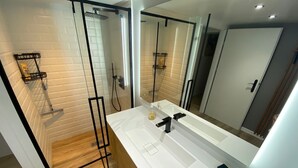 A modern bathroom with a glass-enclosed shower, a white vanity with a large mirror, and wooden flooring.