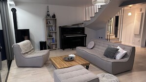 A modern living room with a grey sofa, two armchairs, a wooden coffee table, and a black piano.