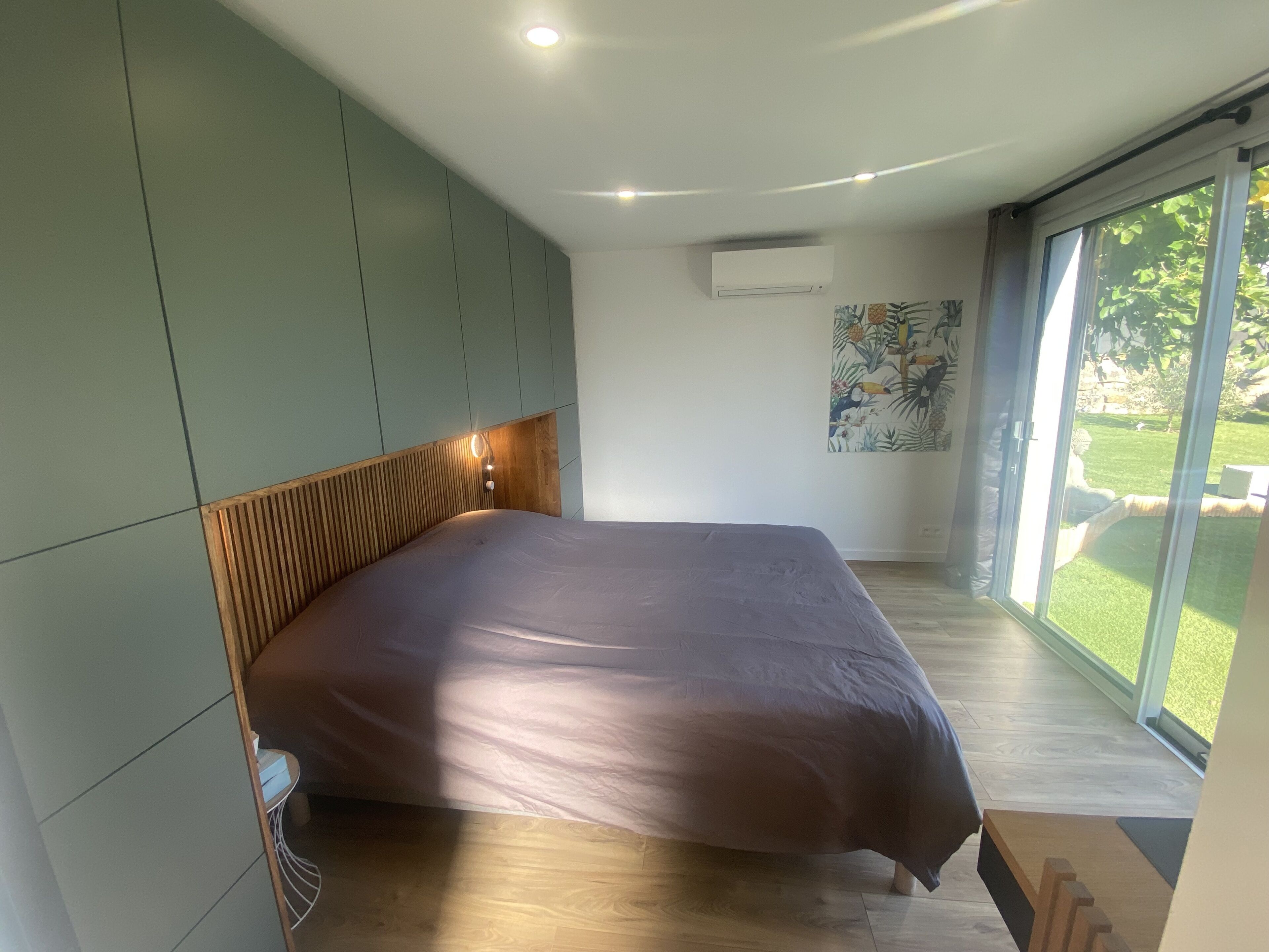 Un dormitorio moderno con una cama grande, armarios empotrados y vistas a un jardín por una puerta corrediza de vidrio.