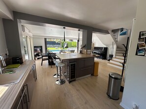 A modern kitchen with a central island, bar stools, a piano, and a view of a garden.