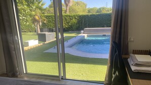A room with a large sliding glass door leading to a swimming pool, a bed, a desk with a chair, and a radiator.