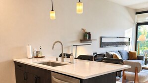 Una cocina moderna con lavavajillas, pileta y horno empotrado. Hay una zona de comedor con sofá y mesa de centro.