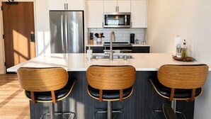 Una cocina moderna con una isla central, electrodomésticos de acero inoxidable y taburetes de bar de madera.
