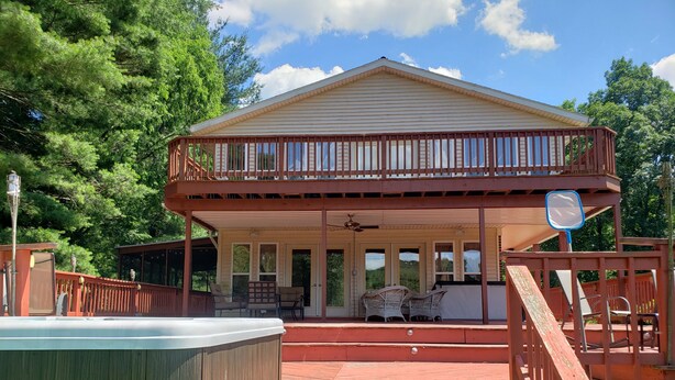 Una casa de madera de dos pisos con balcón, jacuzzi y un patio cubierto con mobiliario exterior.