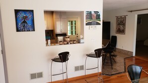 Una cocina moderna con ventana, un área de comedor con dos taburetes tipo barra y un salón con sofá y mesa de centro.