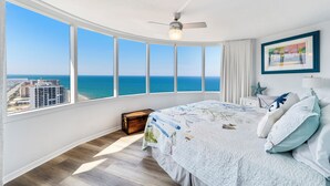 A bedroom with a large window offering a view of the ocean and buildings.