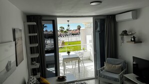 Una sala de estar moderna con un sofá, un televisor y un balcón con mesa y sillas.